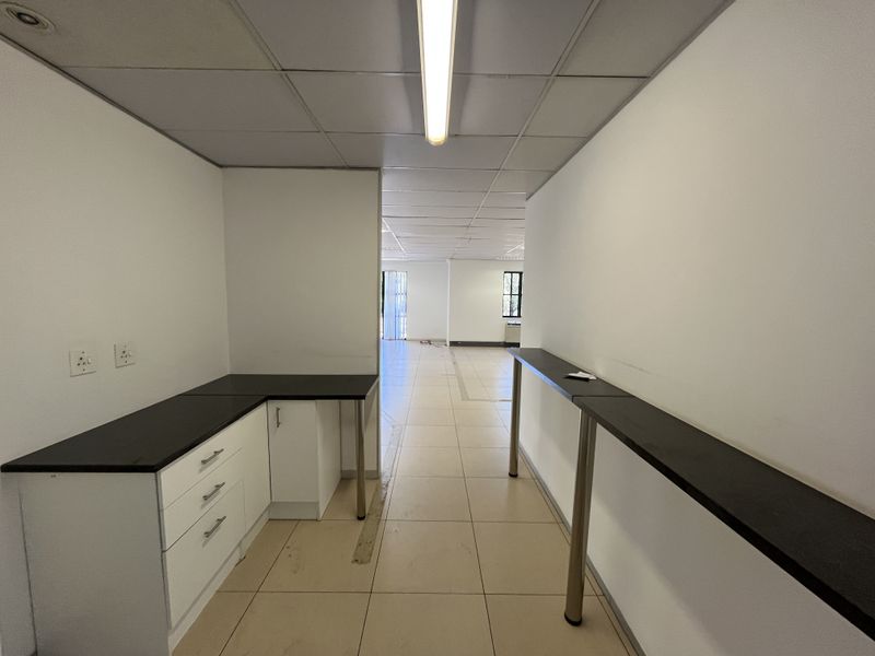 An empty office space featuring tiled flooring, a suspended ceiling, built-in cabinetry with a dark countertop, and a long wall-mounted desk surface.