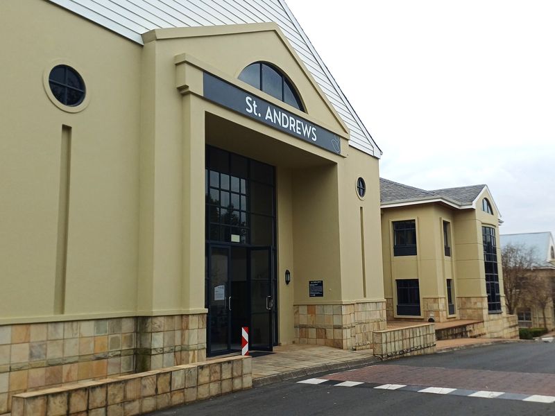 Front exterior view of the St. Andrews office building featuring stone cladding, large glass entrance, and a paved driveway approach.