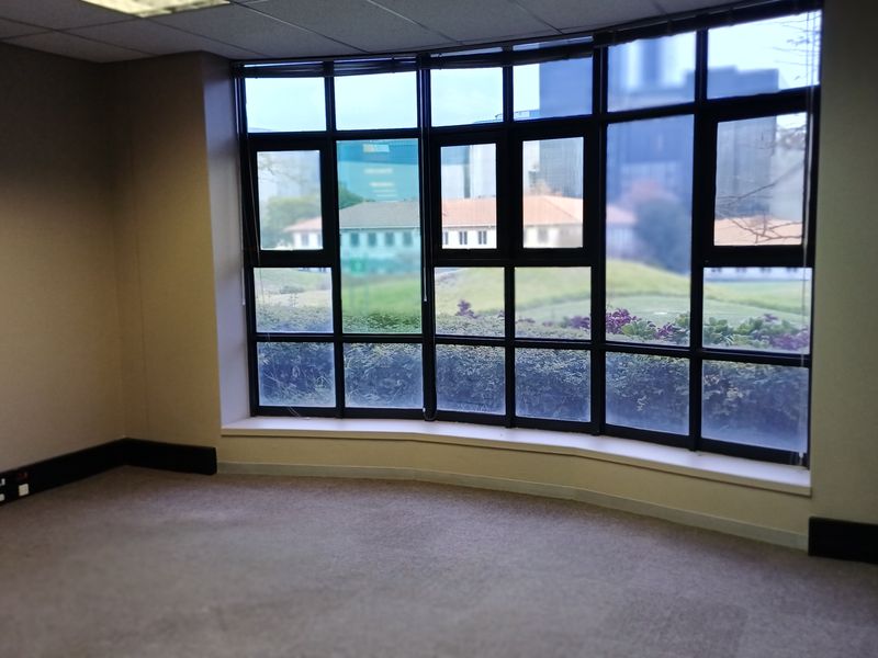 A vacant office space featuring a large bay window with natural light, carpeted flooring, and integrated electrical trunking.