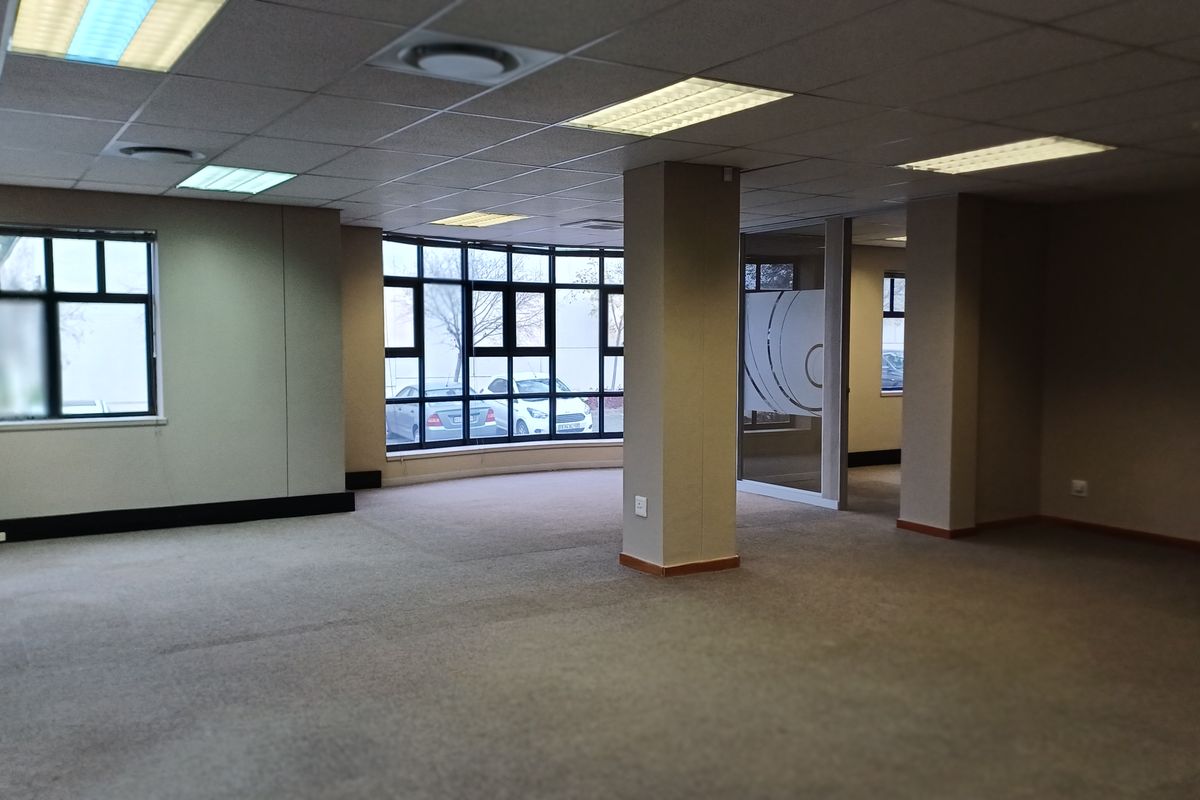 Spacious open-plan office area featuring neutral carpeting, suspended ceilings with recessed lighting, and large windows providing ample natural light.