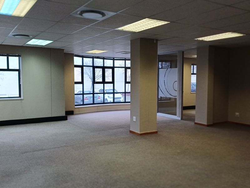 Spacious open-plan office area featuring neutral carpeting, suspended ceilings with recessed lighting, and large windows providing ample natural light.