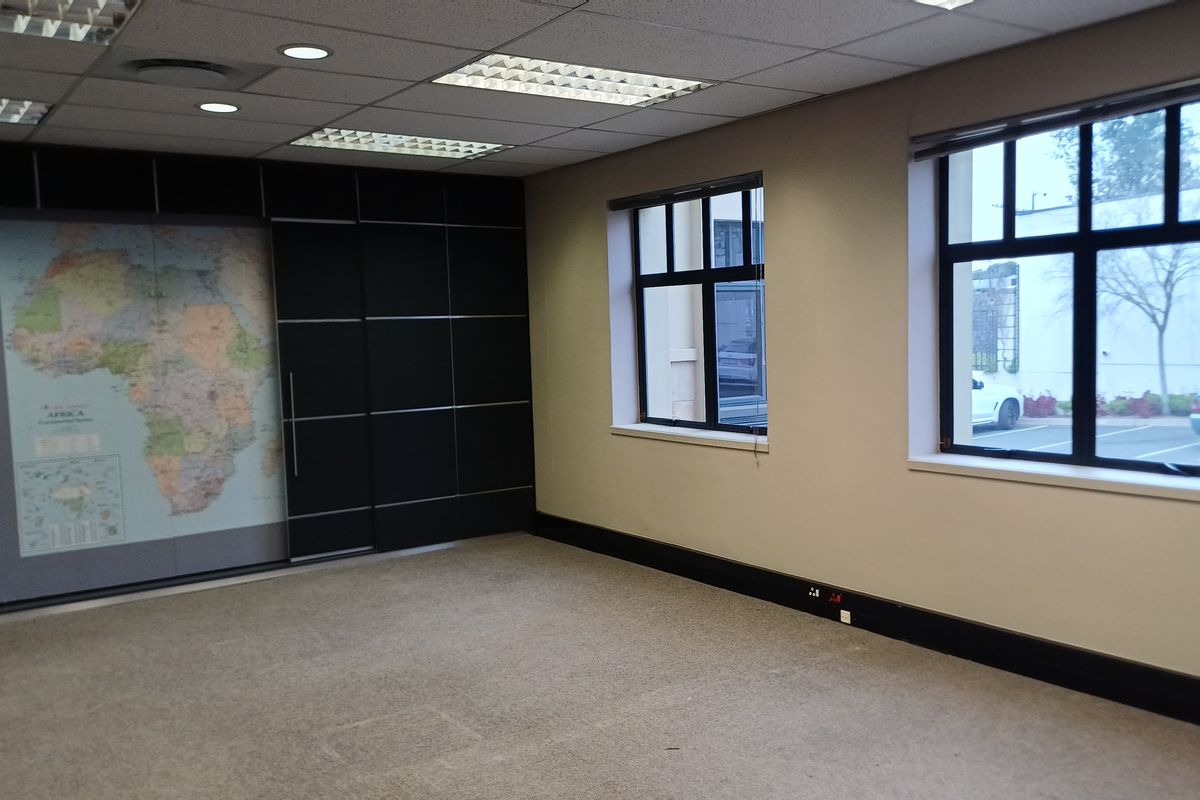 A vacant office space featuring neutral carpeting, a suspended ceiling with recessed lighting, and dark feature wall paneling with large windows.