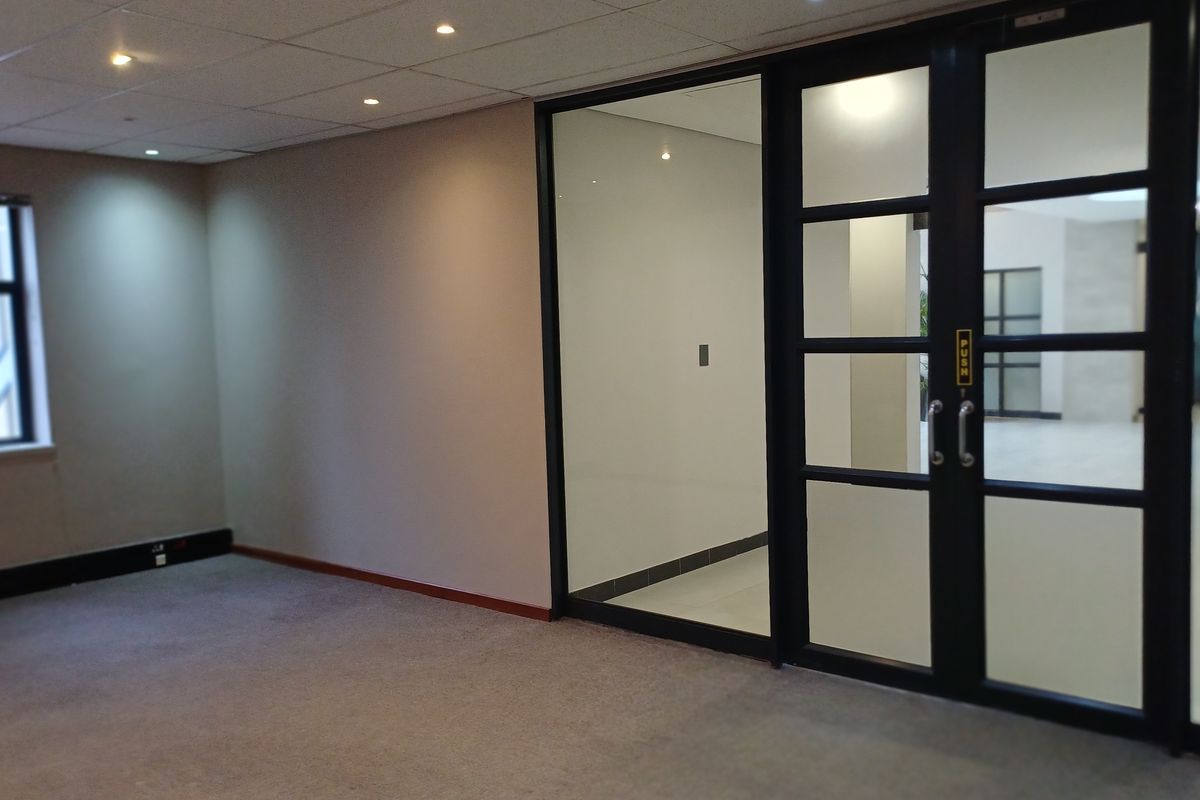 A clean, vacant office space featuring a modern glass partition, suspended ceiling with recessed lighting, and neutral carpet flooring.