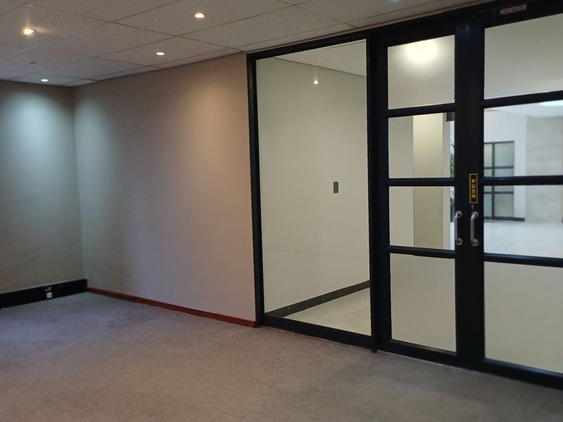 A clean, vacant office space featuring a modern glass partition, suspended ceiling with recessed lighting, and neutral carpet flooring.