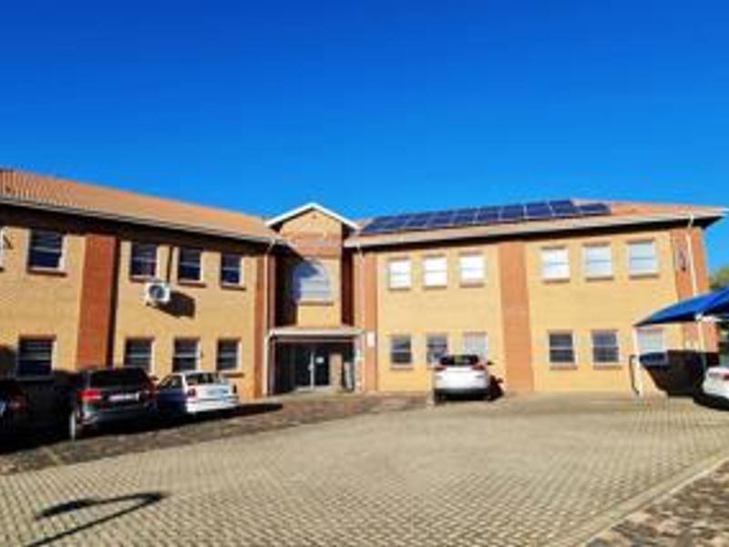 Front exterior view of a two-story office building featuring a brick facade, tiled roof, solar panels, and a paved parking area.