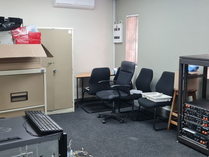 A functional office space featuring carpet flooring, vertical blinds, and a wall-mounted split-system air conditioner.