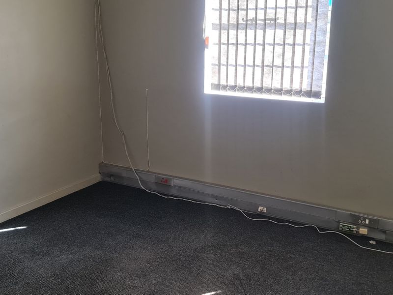 A vacant office space featuring dark carpet flooring, wall-mounted electrical trunking, and vertical window blinds.
