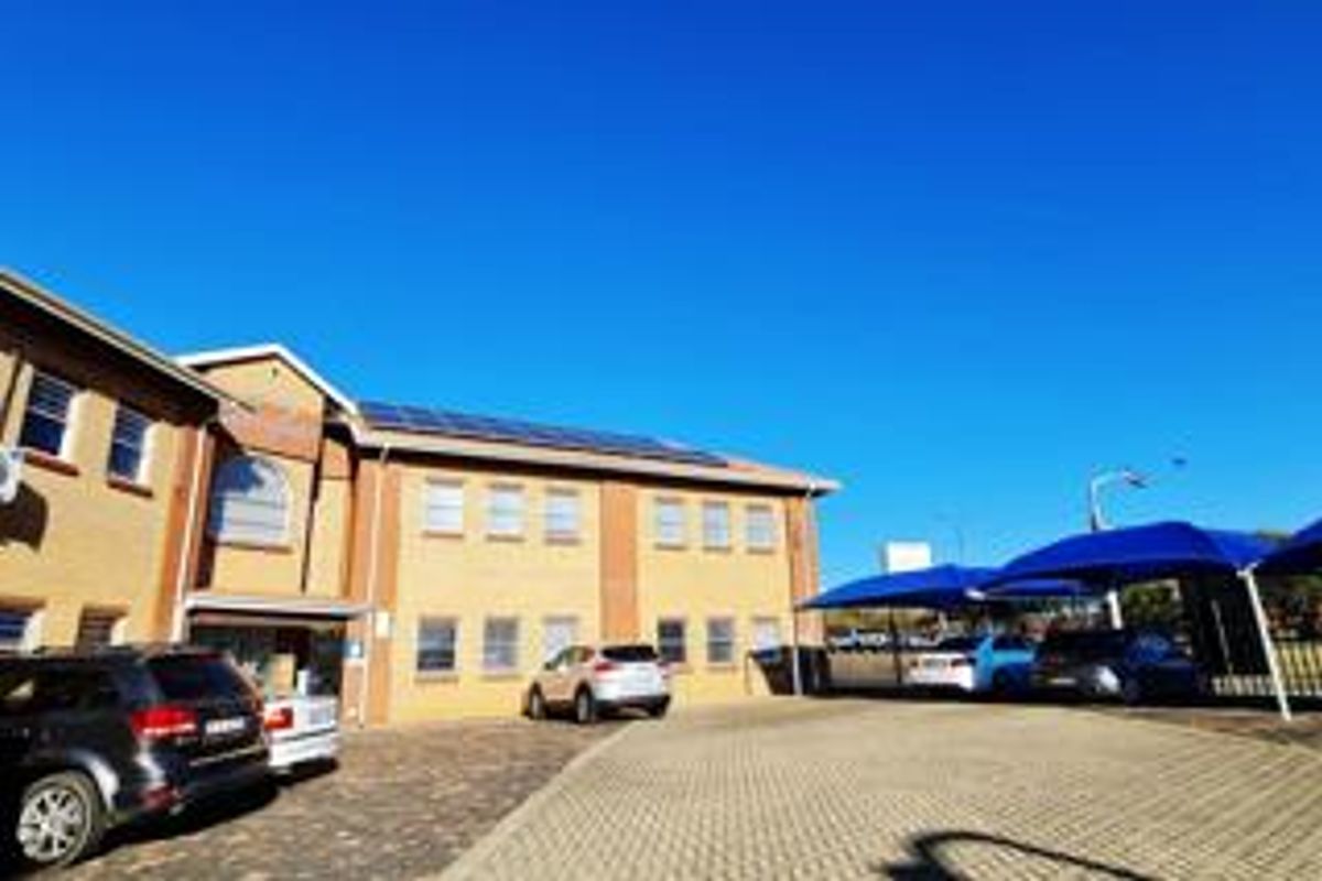 Front exterior view of a commercial office building featuring a brick facade, paved parking area, and installed solar panels on the roof.
