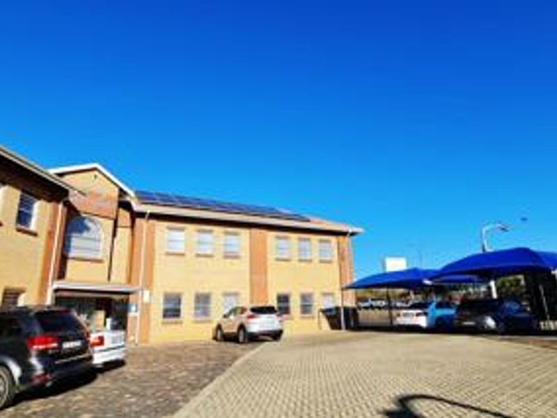 Front exterior view of a commercial office building featuring a brick facade, paved parking area, and installed solar panels on the roof.