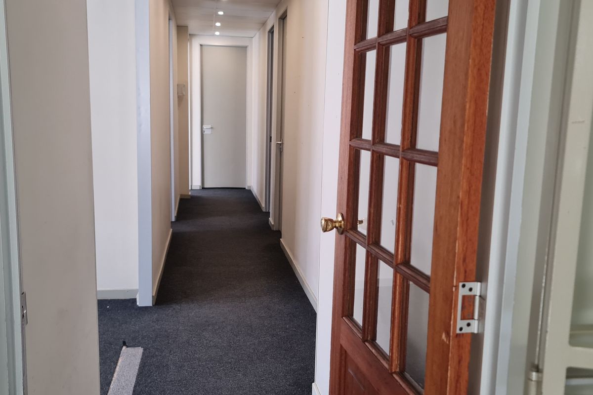 A functional office hallway featuring dark carpeting, recessed lighting, and a classic timber-framed glass door leading to adjacent office spaces.