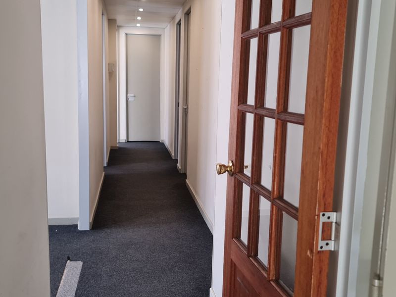 A functional office hallway featuring dark carpeting, recessed lighting, and a classic timber-framed glass door leading to adjacent office spaces.