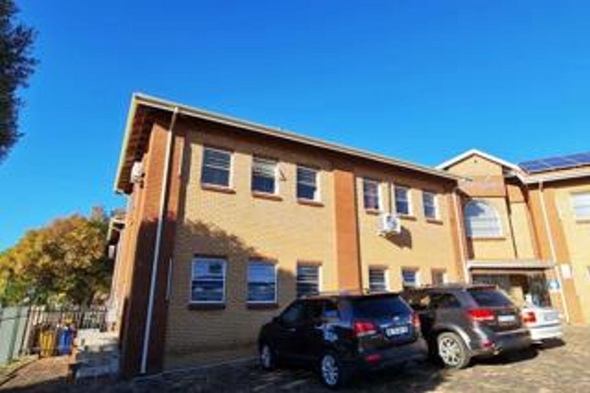 A view of the front exterior of a brick office building featuring a paved driveway and installed air conditioning units.