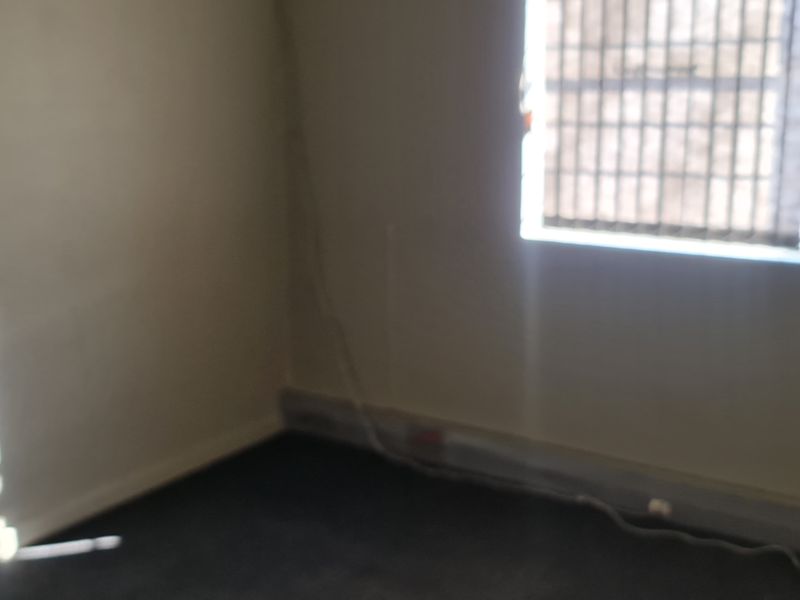 An empty office space featuring a window with security bars and visible electrical trunking along the base of the wall.