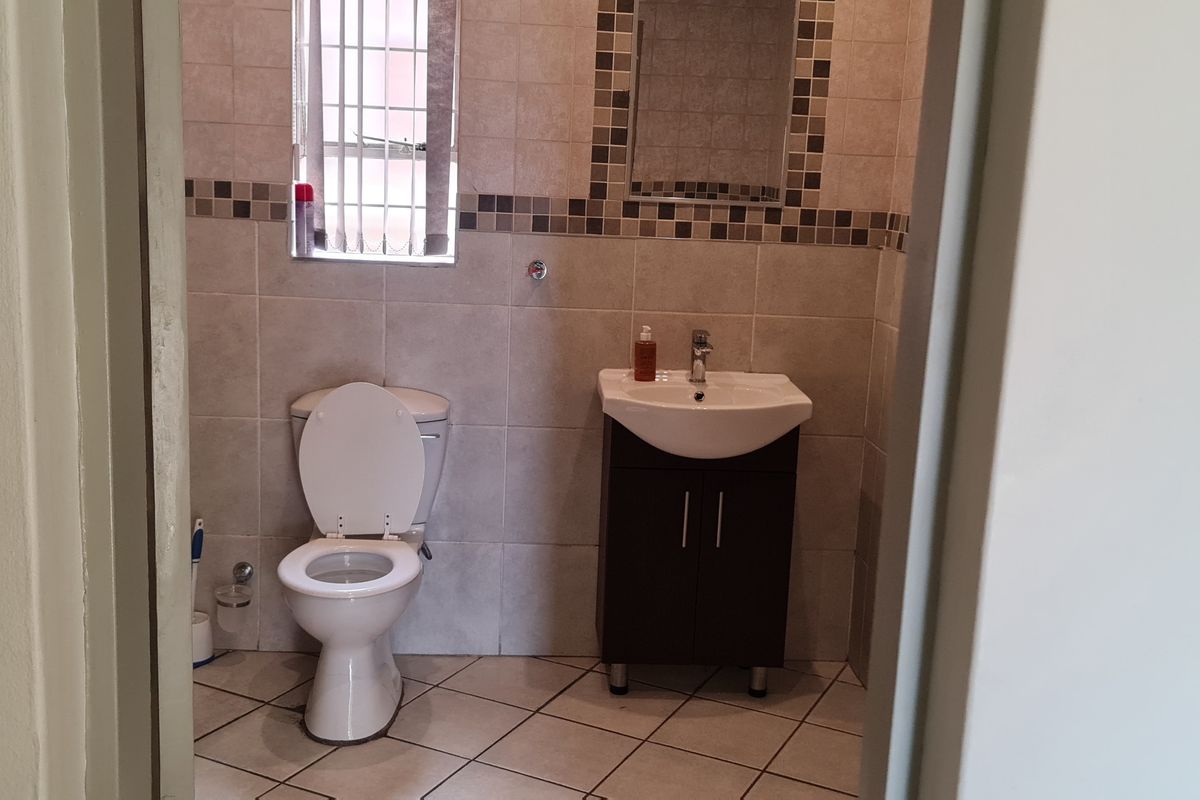 A functional bathroom featuring tiled walls and floors, a vanity cabinet with a wash basin, and a toilet, viewed from the doorway.