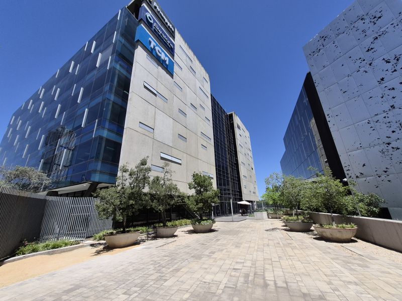 Modern commercial office complex featuring glass curtain walls, concrete facade elements, and a landscaped paved courtyard area.