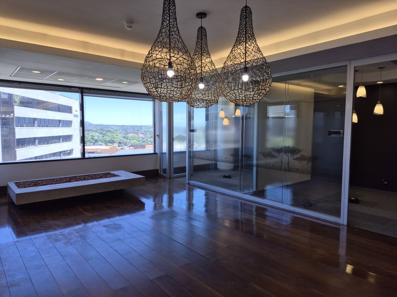 Modern office space featuring polished hardwood floors, glass partitions, recessed lighting, and large windows with expansive city views.