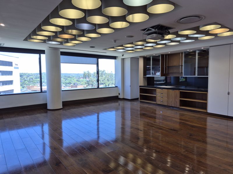 Spacious office area featuring polished hardwood flooring, extensive built-in cabinetry, and a unique circular recessed lighting design with large windows offering city views.