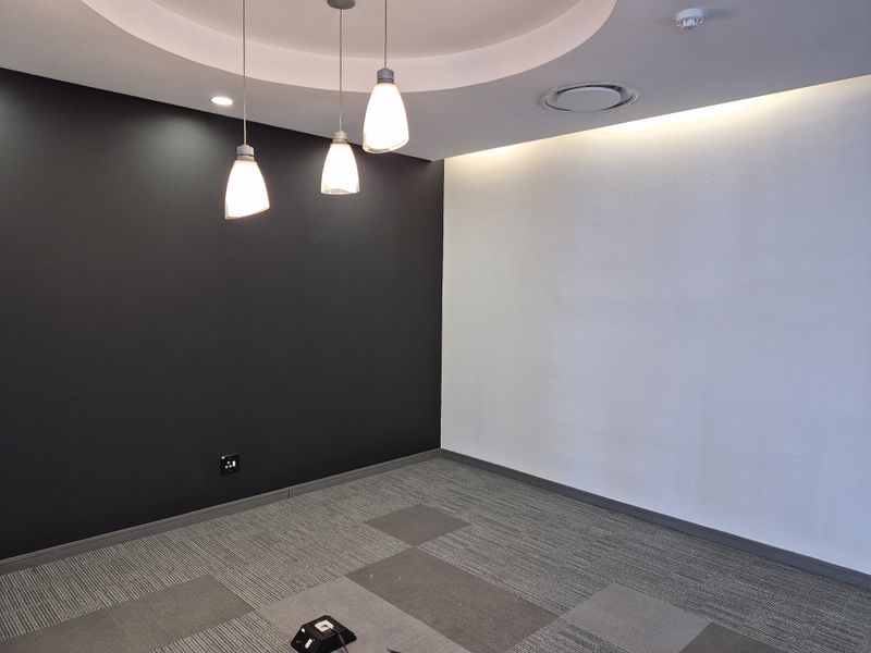 A modern, empty office space featuring a recessed ceiling with cove lighting, pendant lights, and durable grey carpet tiles.