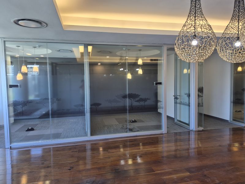 Modern office space featuring glass partition walls, polished hardwood flooring, and sophisticated recessed and pendant lighting fixtures.