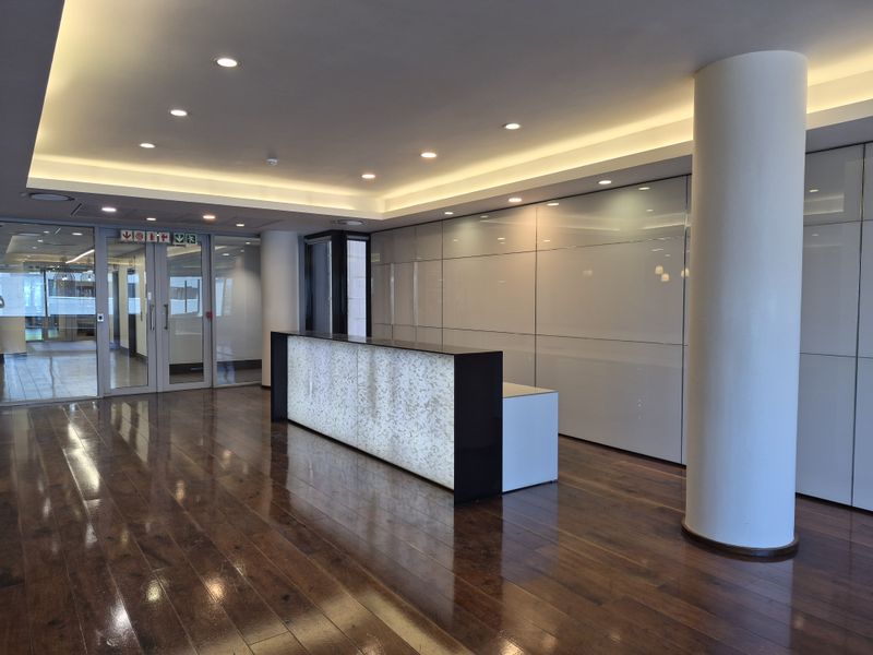 Modern office reception area featuring polished hardwood flooring, a backlit reception desk, integrated wall cabinetry, and professional recessed lighting.