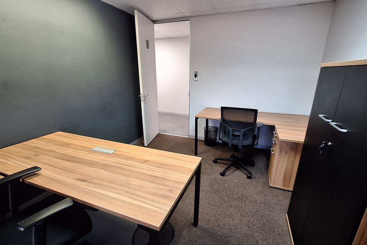 A functional office space featuring carpeted flooring, a suspended ceiling, and a neutral color palette with a dark accent wall.