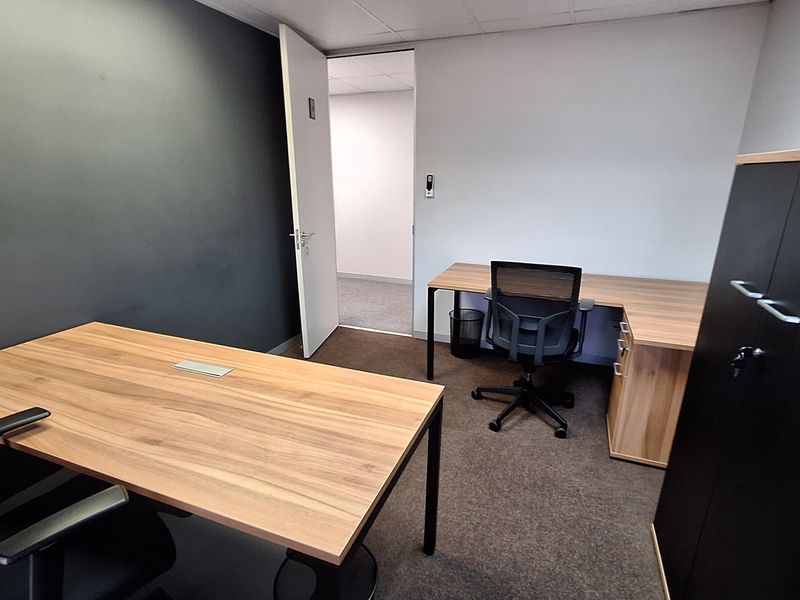 A functional office space featuring carpeted flooring, a suspended ceiling, and a neutral color palette with a dark accent wall.