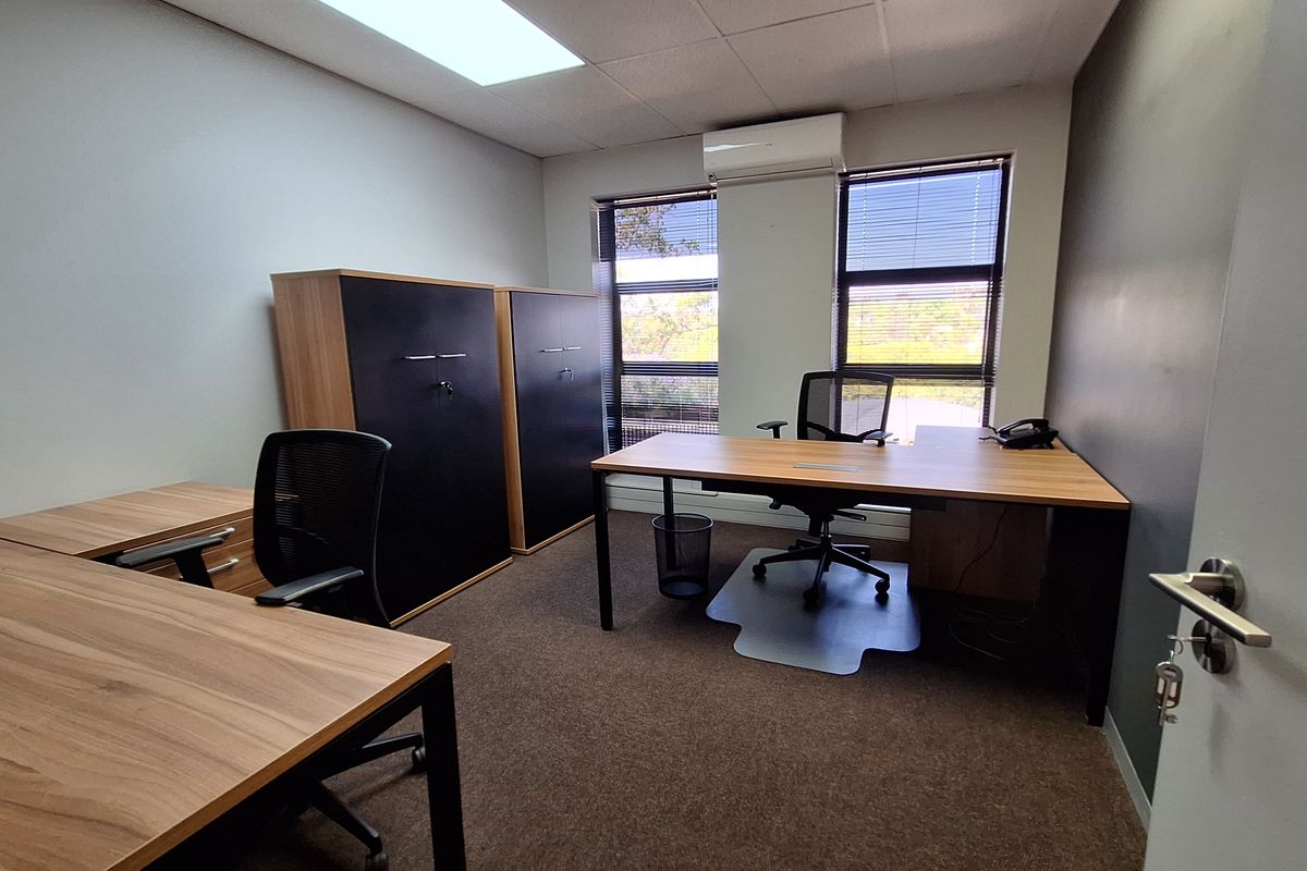 A professional office space featuring carpeted flooring, a drop ceiling with recessed lighting, and a wall-mounted split-system air conditioning unit.