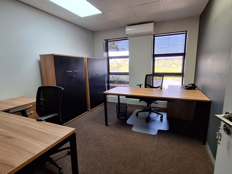 A professional office space featuring carpeted flooring, a drop ceiling with recessed lighting, and a wall-mounted split-system air conditioning unit.