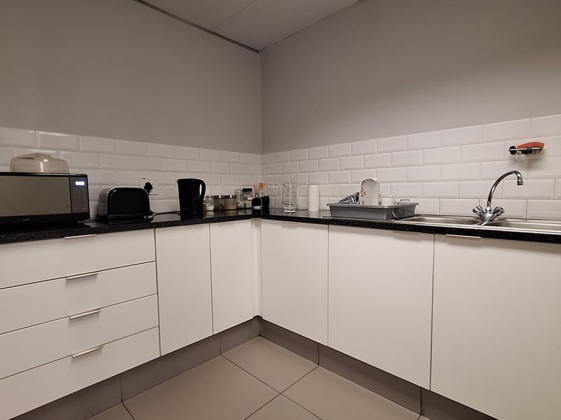 A clean and functional office kitchenette featuring white cabinetry, a dark countertop, a stainless steel sink, and a classic white subway tile backsplash.