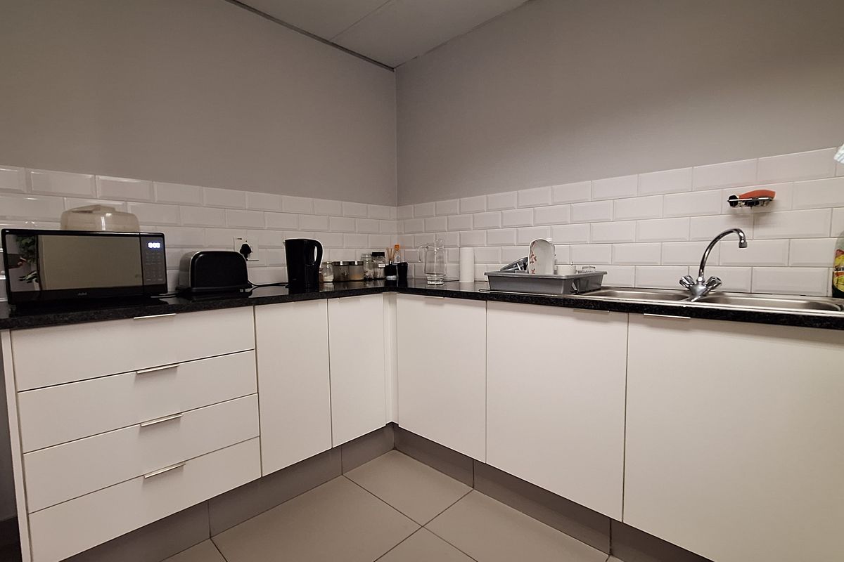 A clean and functional office kitchenette featuring white cabinetry, a dark countertop, a stainless steel sink, and a classic white subway tile backsplash.