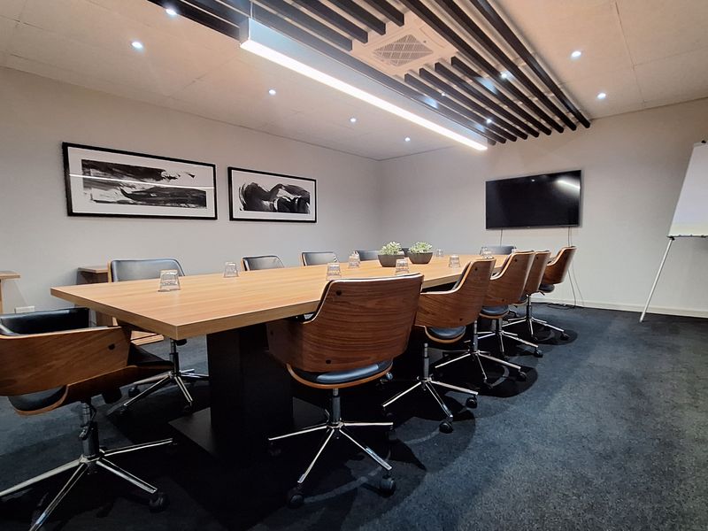 A professional boardroom featuring a large meeting table, wall-mounted display, and modern slatted ceiling design with recessed lighting.