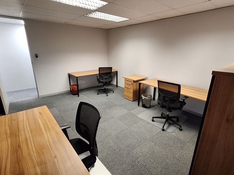 A functional office space featuring carpet tiles, a suspended ceiling with recessed lighting, and multiple workstations.