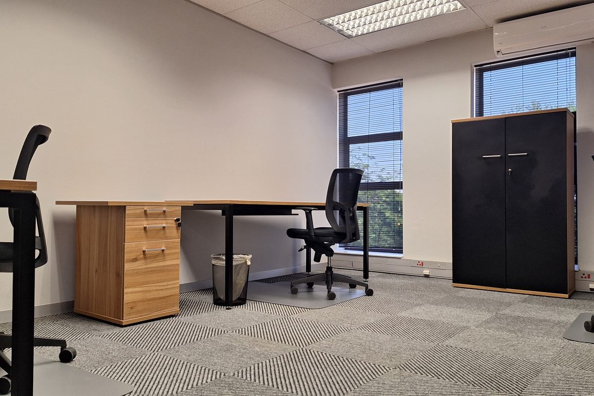A professional office space featuring carpeted flooring, suspended ceilings with recessed lighting, and a wall-mounted air conditioning unit.