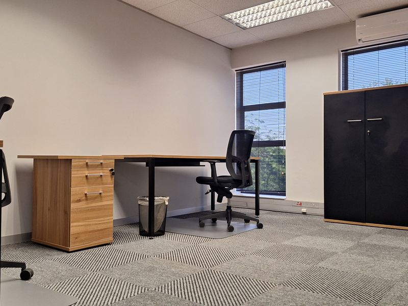 A professional office space featuring carpeted flooring, suspended ceilings with recessed lighting, and a wall-mounted air conditioning unit.