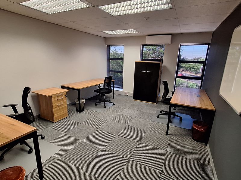 A well-lit office space featuring carpeted flooring, suspended ceiling tiles, air conditioning, and large windows providing natural light.