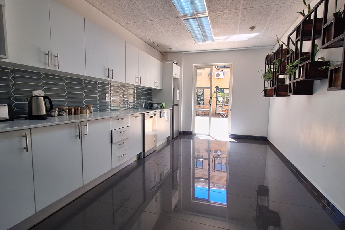 Modern office kitchen featuring sleek white cabinetry, tiled backsplash, polished floor tiles, and direct access to an outdoor area.
