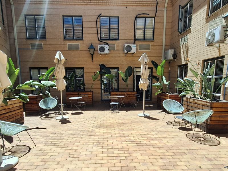 A paved outdoor courtyard area featuring brick walls, multiple air conditioning units, and wall-mounted lighting fixtures, suitable for office break-out space.