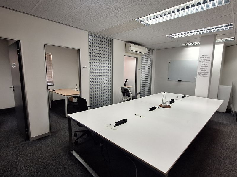 A professional office space featuring a large central desk, suspended ceiling with recessed lighting, wall-mounted air conditioning, and integrated internal office partitions.