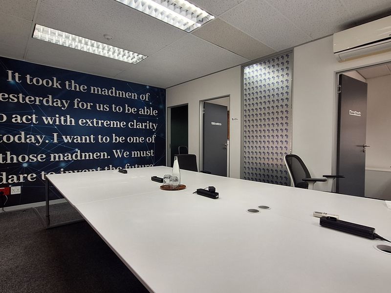 A professional office meeting room featuring a large built-in desk, suspended ceiling with integrated lighting, and wall-mounted air conditioning.