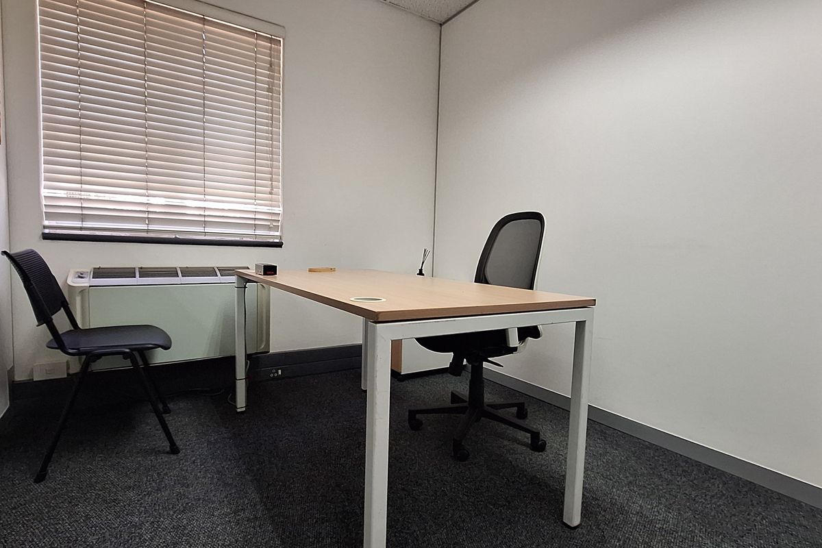 A functional private office space featuring carpeted flooring, a window with blinds, and a built-in HVAC unit.