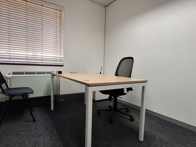 A functional private office space featuring carpeted flooring, a window with blinds, and a built-in HVAC unit.