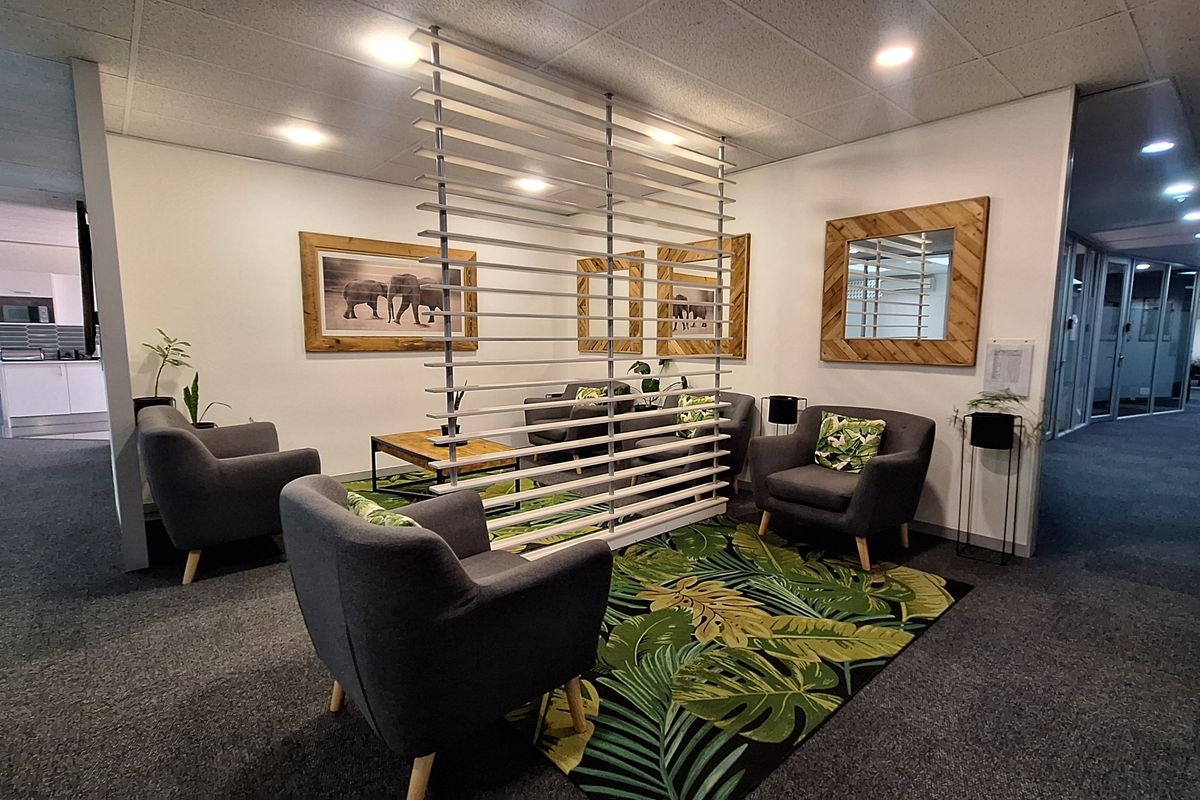 A professional office waiting area featuring a modern slatted partition screen, recessed ceiling lighting, and carpeted flooring.