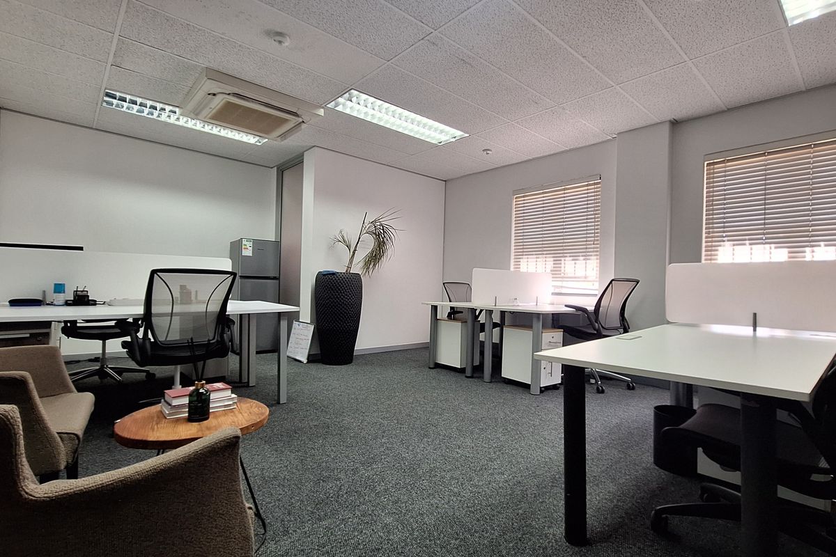 A functional office space featuring carpeted flooring, suspended ceilings with recessed lighting, integrated air conditioning, and large windows with venetian blinds.