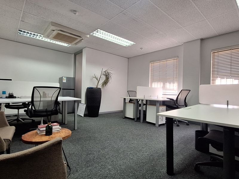 A functional office space featuring carpeted flooring, suspended ceilings with recessed lighting, integrated air conditioning, and large windows with venetian blinds.
