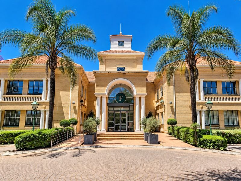 A professional front elevation view of a well-maintained office building featuring classic architectural details, a grand arched entrance, and manicured landscaping.