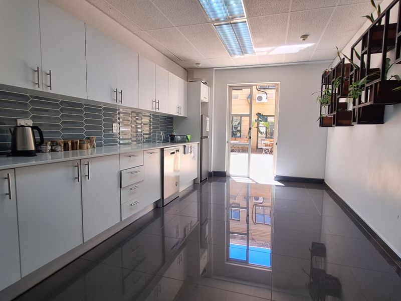 Modern office kitchen featuring sleek white cabinetry, tiled backsplash, polished floor tiles, and direct access to an outdoor area.