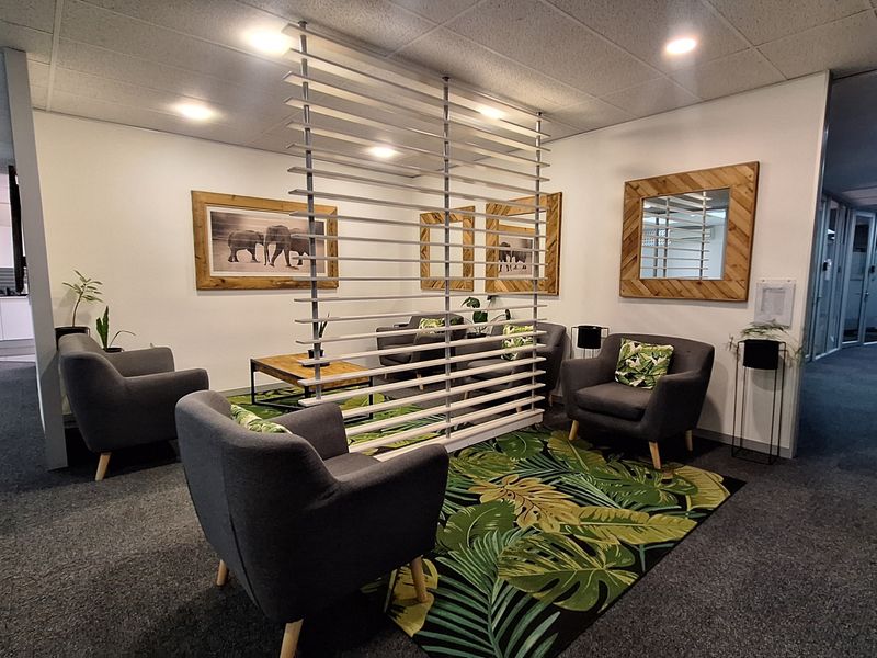 A professional office waiting area featuring a modern slatted partition screen, recessed ceiling lighting, and carpeted flooring.