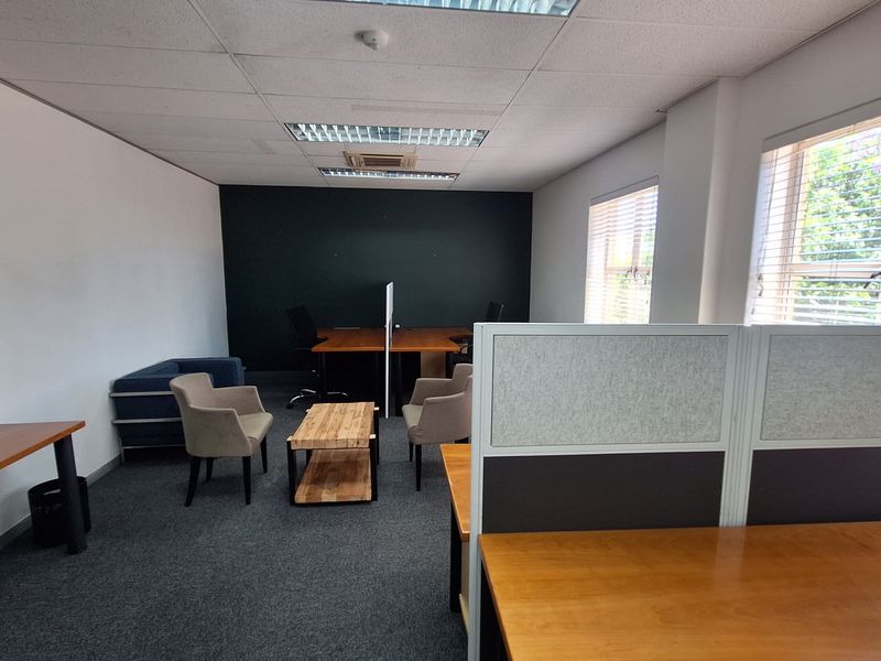 A functional office space featuring carpeted flooring, suspended ceilings with recessed lighting, and large windows with venetian blinds for natural light.