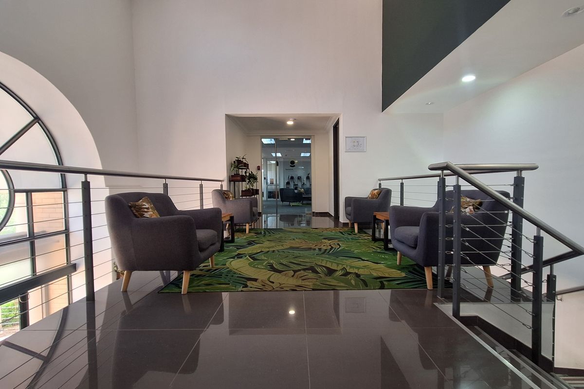 A modern office hallway featuring polished tiled flooring, a stainless steel balustrade, and an arched window providing natural light.