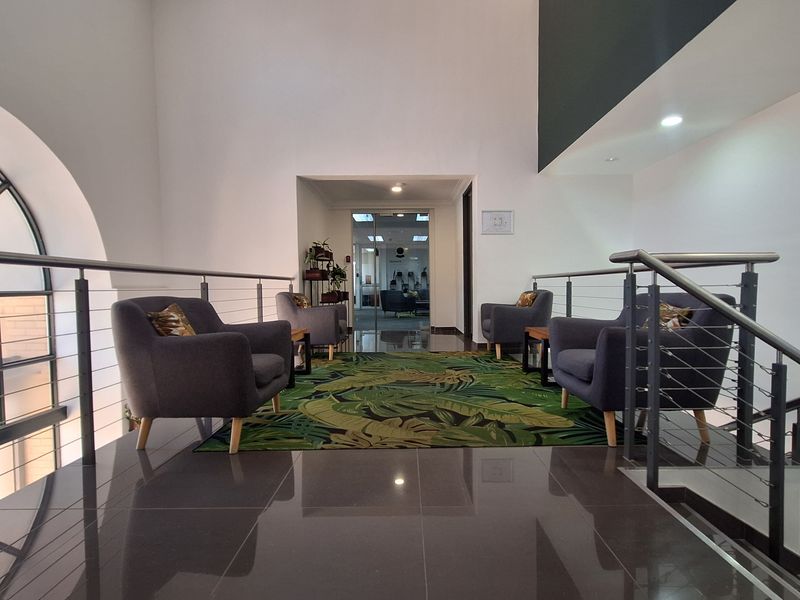 A modern office hallway featuring polished tiled flooring, a stainless steel balustrade, and an arched window providing natural light.
